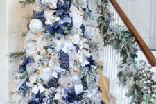 a stylish Christmas tree with silver and white ornaments, navy ribbons and poinsettias, berries and lights is wow