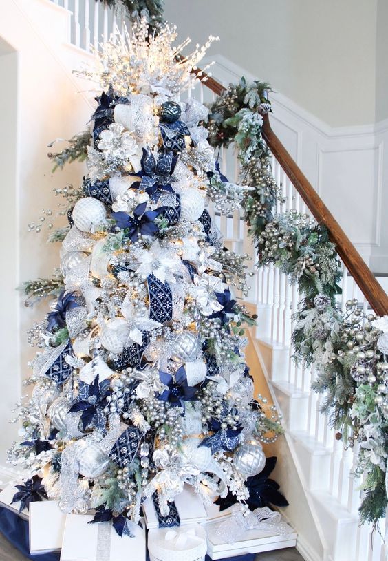 a stylish Christmas tree with silver and white ornaments, navy ribbons and poinsettias, berries and lights is wow