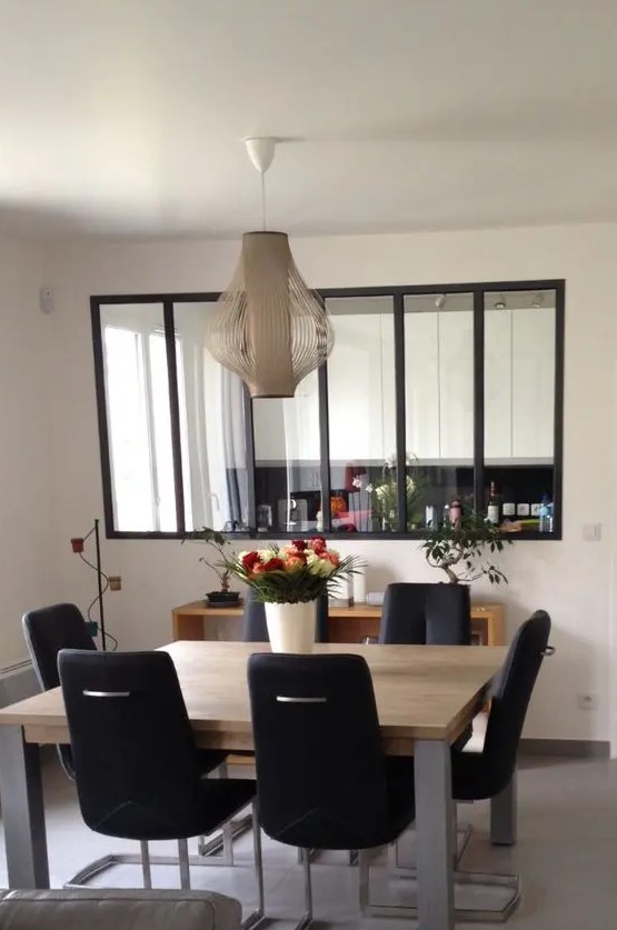 a stylish modern dining space with a large interior window with black frames that connects the space with the kitchen