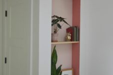 a stylish niche painted pink, with thin wooden shelves, potted plants, books and a green light over it is a lovely color accent for a mid-century modern interior
