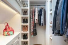 a tall and narrow white closet with lots of shelves, open storage compartments, railings for clothes and built-in lights