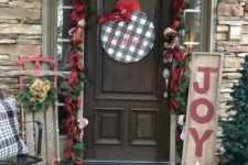a vintage farmhouse Christmas porch with plaid ribbons, evergreens, a plaid sign, vine gifts and pillows plus a decorated sleigh