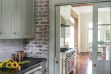 a vintage kitchen with light green cabinets, black countertops, brick walls and a door with a transom window over it