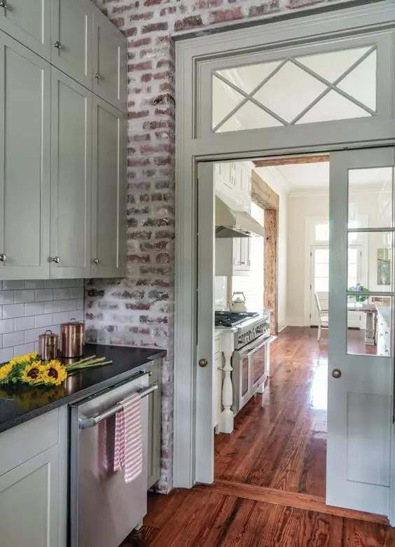 a vintage kitchen with light green cabinets, black countertops, brick walls and a door with a transom window over it
