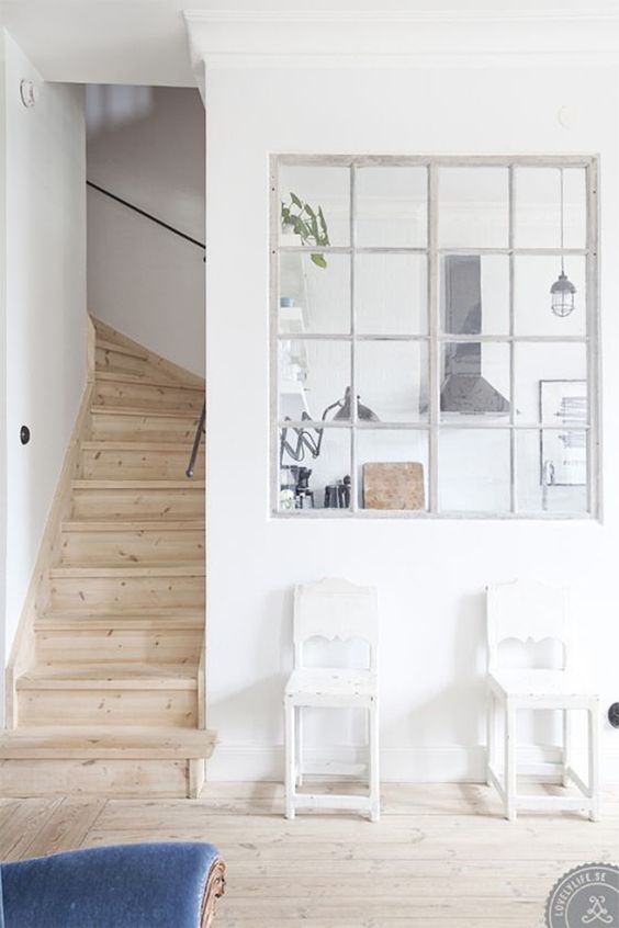 a white Scandinavian space with an interior window that lets natural light flow from the kitchen to the entryway