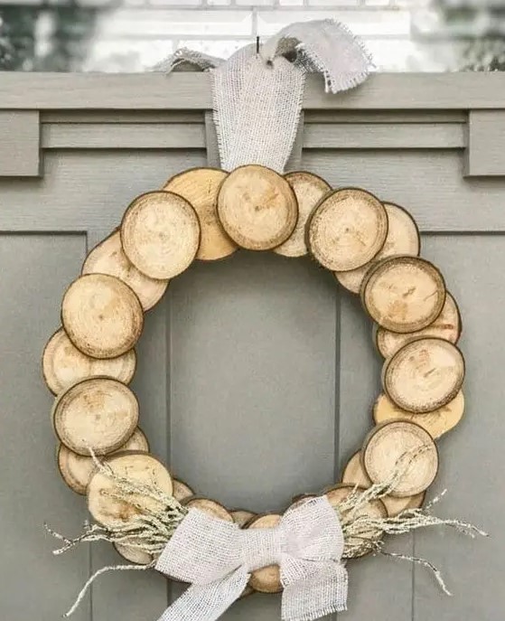 a wood slice Christmas wreath with a burlap bow and some dried herbs for a natural feel