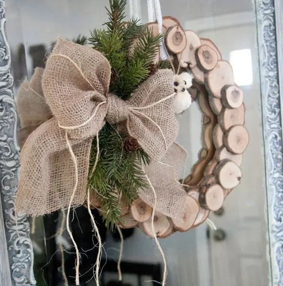 a wood slice Christmas wreath with evergreens, pinecones and a large burlap bow on the side