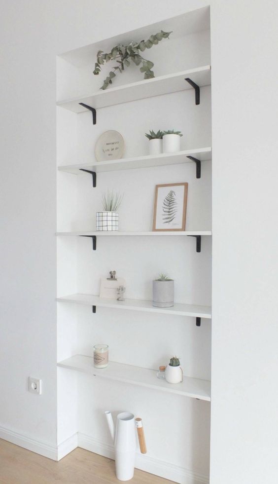 an airy minimalist space with built-in niche shelves with various decor and potted greenery is a lovely one