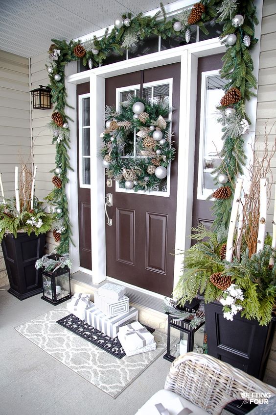 an elegant Christmas porch with evergreens, pinecones, ornaments, arrangements in planters and gift boxes and candle lanterns