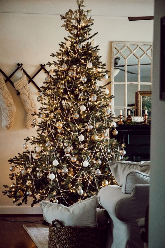an elegant and gold-fashioned Christmas tree decorated with white and metallic ornaments, beads and lights plus leaves on top
