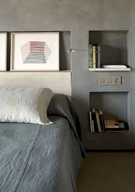 an industrial bedroom with concrete walls and niche shelves instead of nightstands, this is a great alternative to usual shelves and they look sleek