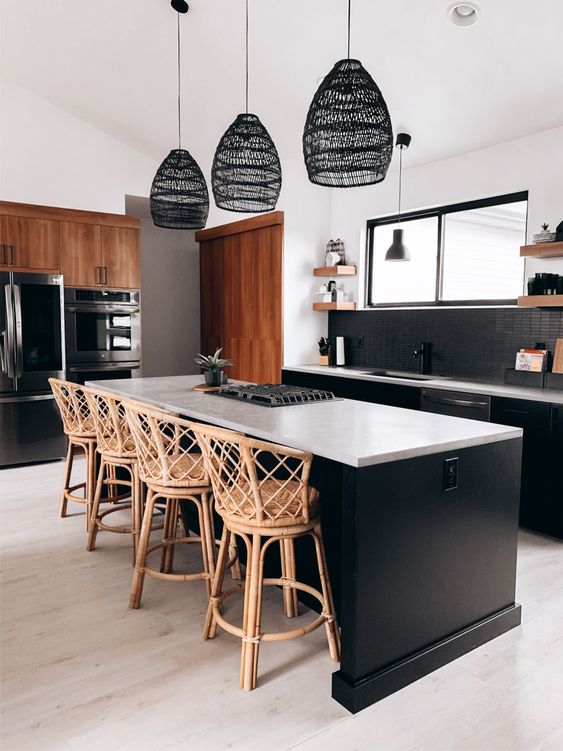a beautiful black kitchen with a black skinny tile backsplash, white countertops, woven stools and lamps