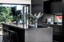 04 a contemporary moody kitchen with sleek black cabinetry, a kitchen island, a glazed wall with an entrance to a courtyard