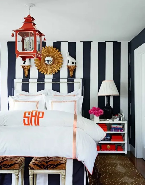 an eye-catchy bedroom with a black and white verticla stripe wall, a canopy bed with neutral bedding, a dresser, some lamps and a red pendant lamp
