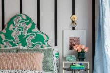 07 a catchy bedroom with a striped accent wall, a green upholstered bed, printed bedding, a chic nightstand with decor