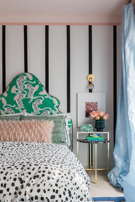 a catchy bedroom with a striped accent wall, a green upholstered bed, printed bedding, a chic nightstand with decor