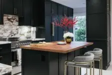 09 a refined black kitchen with a white marble backsplash, a black kitchen island with a butcherblock countertop plus grey stools