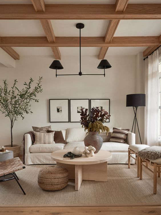a soothing and cozy neutral living room with a creamy sofa, printed pillows, stools, a round table and black lamps