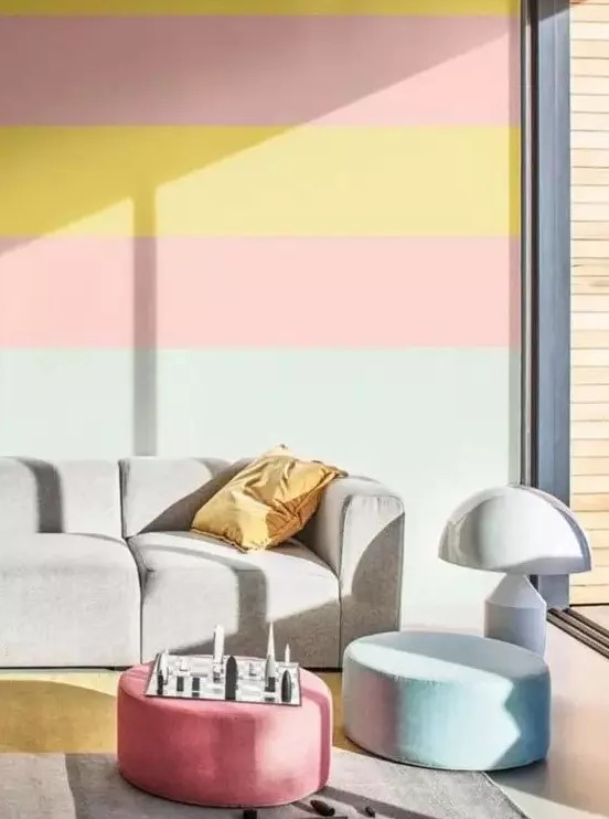 a colorful living room with a bold striped wall, a grey sofa, pastel ottomans and a floor lamp is very welcoming