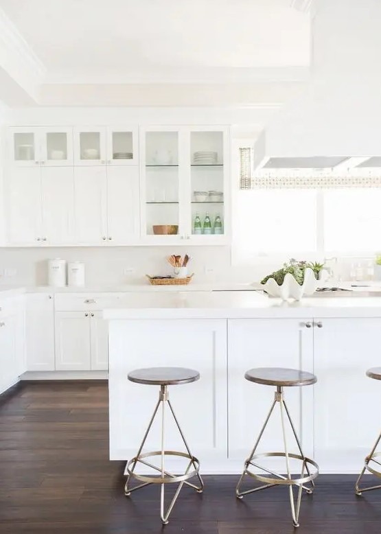 a simple white kitchen with glass cabinets and a large kitchen island leaves an airy feeling