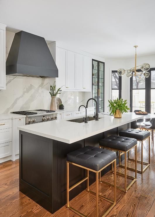 a beautiful white kitchen with shaker cabinets, a grey hood, a black kitchen island with a white countertop and black stools