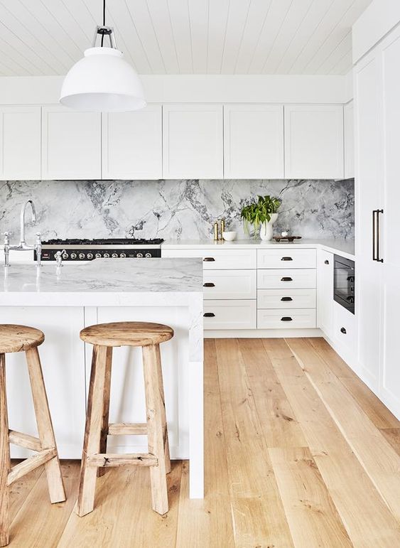 a white contemporary kitchen with shaker cabinets, white marble countertops and a backsplash and wooden stools