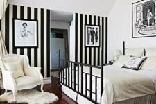 19 a refined vintage bedroom with a black bed and neutral bedding, an accent black and white stripe wall, a neutral chair and a crystal chandelier