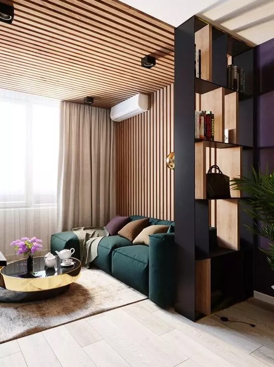 a contemporary living room with a wood slat accent wall, a green low sofa, elegant and shiny coffee tables and a shelving unit space divider
