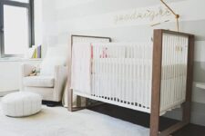 24 an airy neutral nursery with a creamy chair and a pouf, a large crib, a striped grey and white accent wall that brings mor einterest to the space