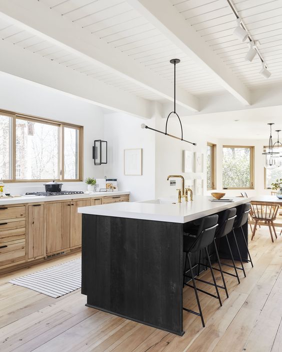 a farmhouse kitchen with timber cabinets, a black kitchen island, white countertops, a catchy pendant lamp and a dining zone