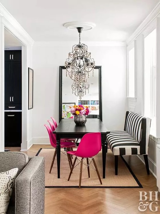 a chic dining space with a statement mirror, a black table, fuchsia chairs, a striped bench and a chic and bold chandelier