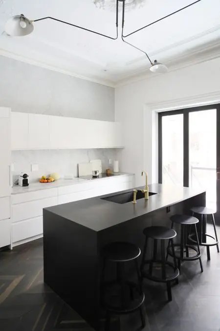 a minimalist black and white kitchen with sleek cabinets, a white stone backsplash, a black kitchen island and stools
