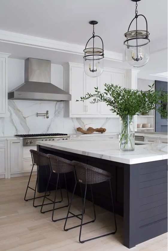 a modern farmhouse kitchen with white shaker style cabinets, a large metal hood, a black kitchen island, a white marble backsplash and countertops