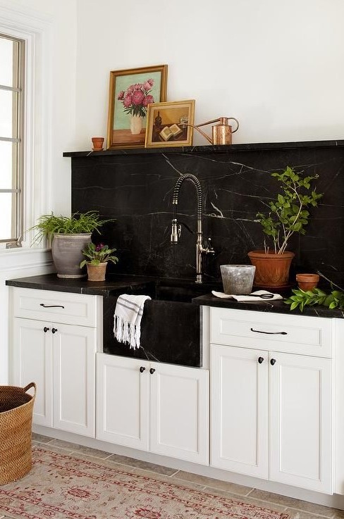 a farmhouse kitchen in white is spruced up and made more eye-catchy with a black marble backsplash and countertops
