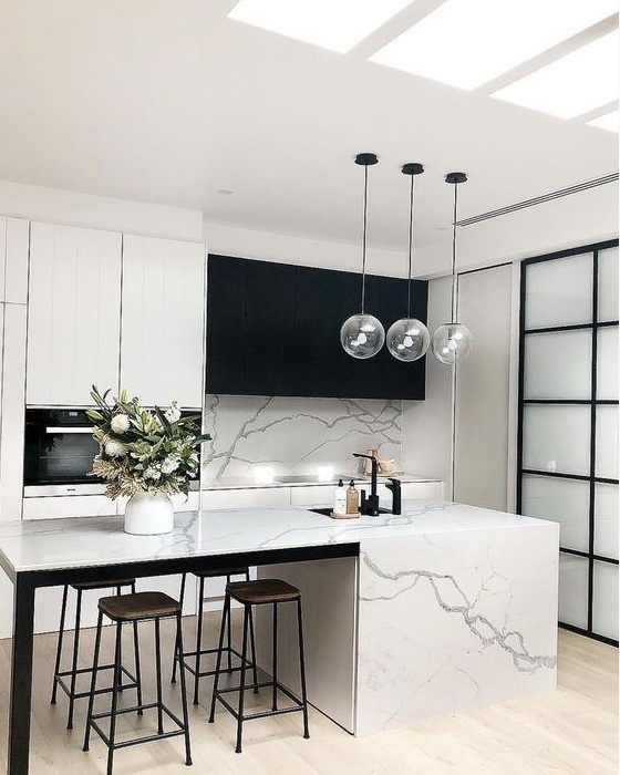 a minimalist contrasting kitchen with black and white cabinets, a white marble tile backsplash and kitchen island plus pendant lamps