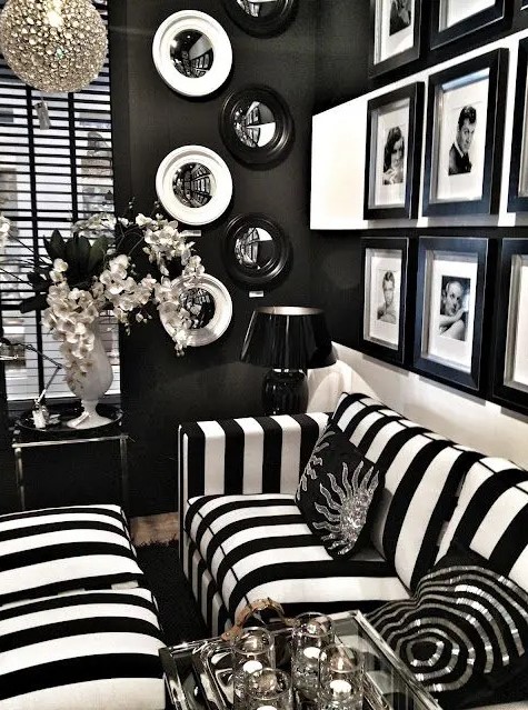 a refined vintage inspired black and white living room with black walls, a black and white strip sofa and poufs, a black and white gallery wall and some decorative plates