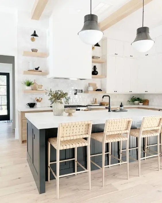a neutral farmhouse kitchen with timber cabinets, white cabinets and open shelves, a black kitchen island, woven stools and black lamps