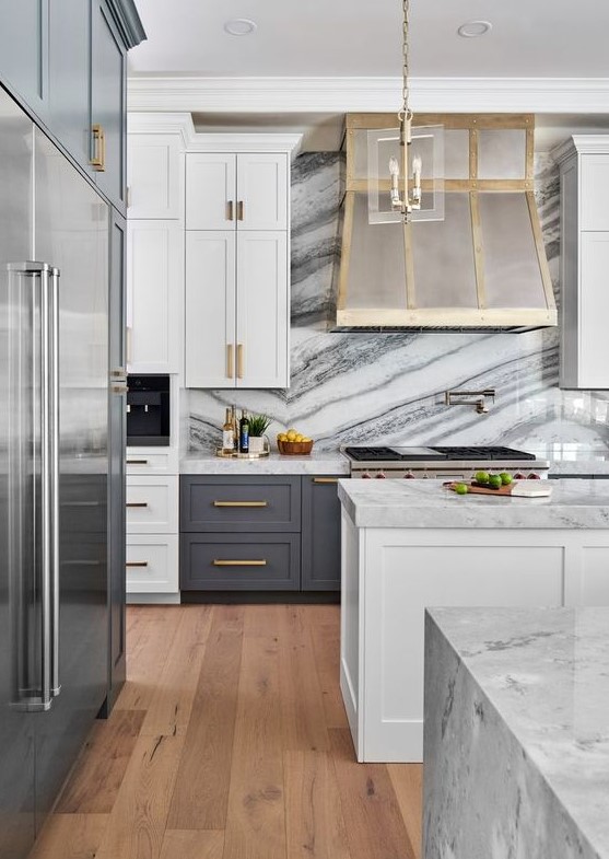 an art deco kitchen with grey and white cabinets, a metal hood, touches of gold and white marble countertops and a backsplash