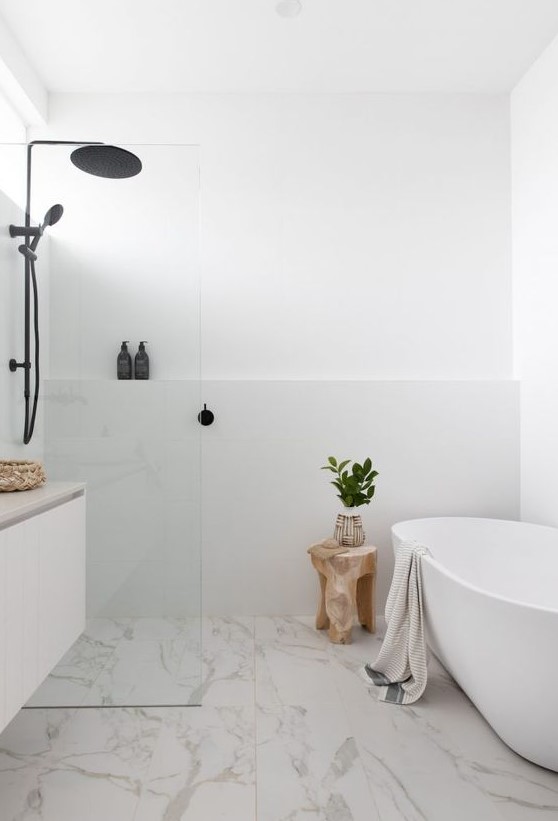 a contemporary white bathroom with white walls, a white marble floor for a catchy touch, an oval tub, a floating vanity and black fixtures
