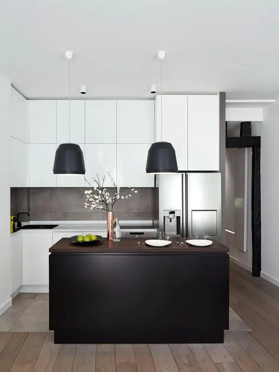 a small black and white kitchen with sleek cabinets, a concrete backsplash, a black kitchen island and black lamps over it