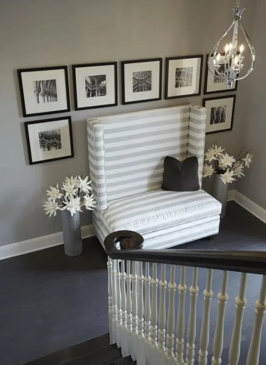 a staircase with a space done with a large loveseat and a tall back plus a black and white gallery wall over it is super elegant
