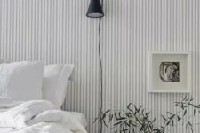 37 a Scandinavian bedroom finished off with a grey and white striped wall, a bed and a nightstand, some greenery and art is welcoming