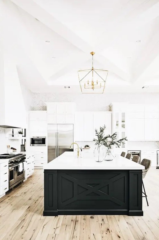 a white modern farmhouse kitchen with shaker cabinets, a black kitchen island, gold touches and greenery
