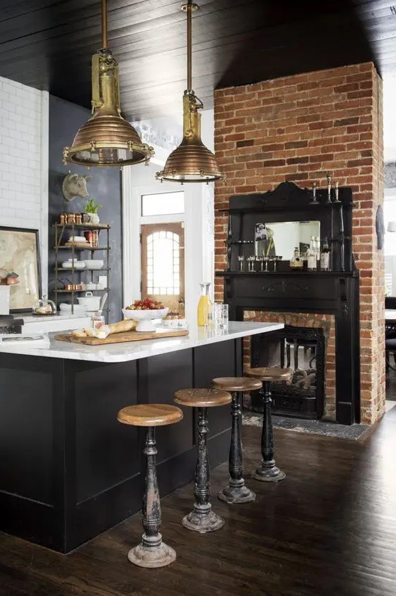 an industrial kitchen with a built-in fireplace, a black kitchen island with a white countertop, tall vintage stools and brass pendant lamps