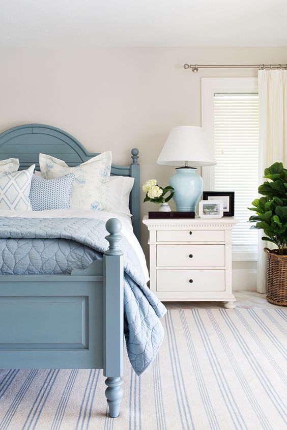 a chic bedroom with a seaside feel, a blue bed with blue and white bedding, an oversized blue striped rug, a white nightstand