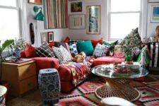 43 a super colorful and bold boho living room with bright layered rugs, a red sofa with colorful pillows and a bold gallery wall