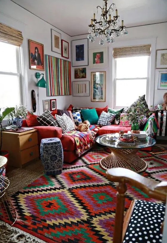 a super colorful and bold boho living room with bright layered rugs, a red sofa with colorful pillows and a bold gallery wall