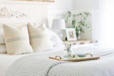 44 a coastal bedroom with a bed with a refined headboard, a large mirror and pillar candles, striped bedding and greenery