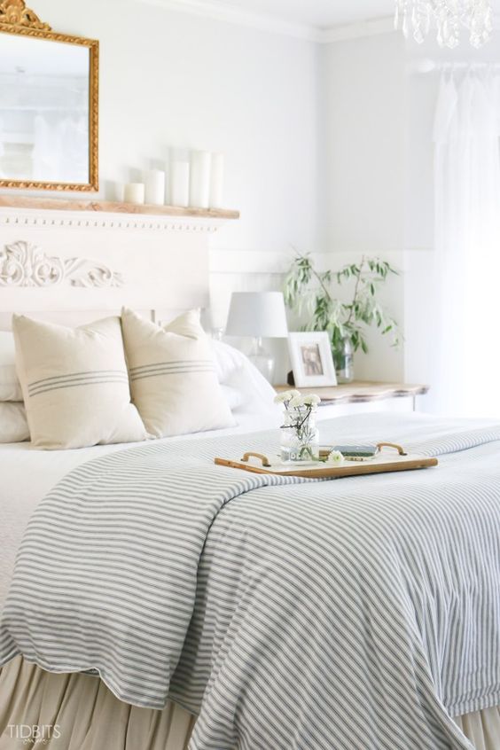 a coastal bedroom with a bed with a refined headboard, a large mirror and pillar candles, striped bedding and greenery