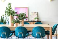 a colorful dining room with a dining table in neutral stain, teal chairs and a pink artwork plus a rug that echoes with both chairs and art